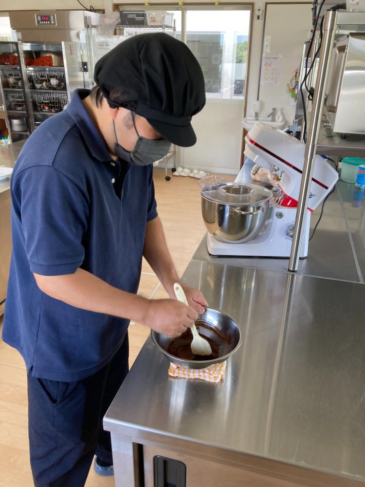 帽子とマスク姿の男性が調理台でボウルの中身をかき混ぜている