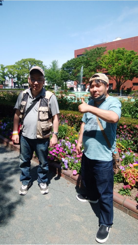 久留米市の石橋文化センター。色とりどりの花が咲いた花壇の前で、男性二人がポーズを決めている