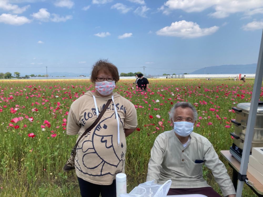 朝倉のキリン花園にて、見渡す限りに広がっているポピーをバックに、にこやかな表情の男女