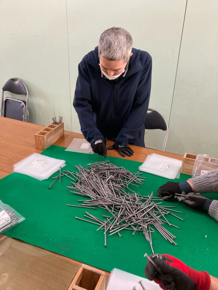 テーブルに積まれた鉄くぎを複数人で囲んで袋詰めしている