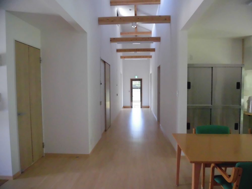 入って左手に延びた廊下。食堂部分も含めて段差のない板張りになっている。壁や天井は白く塗られ、梁は無垢材が使われている